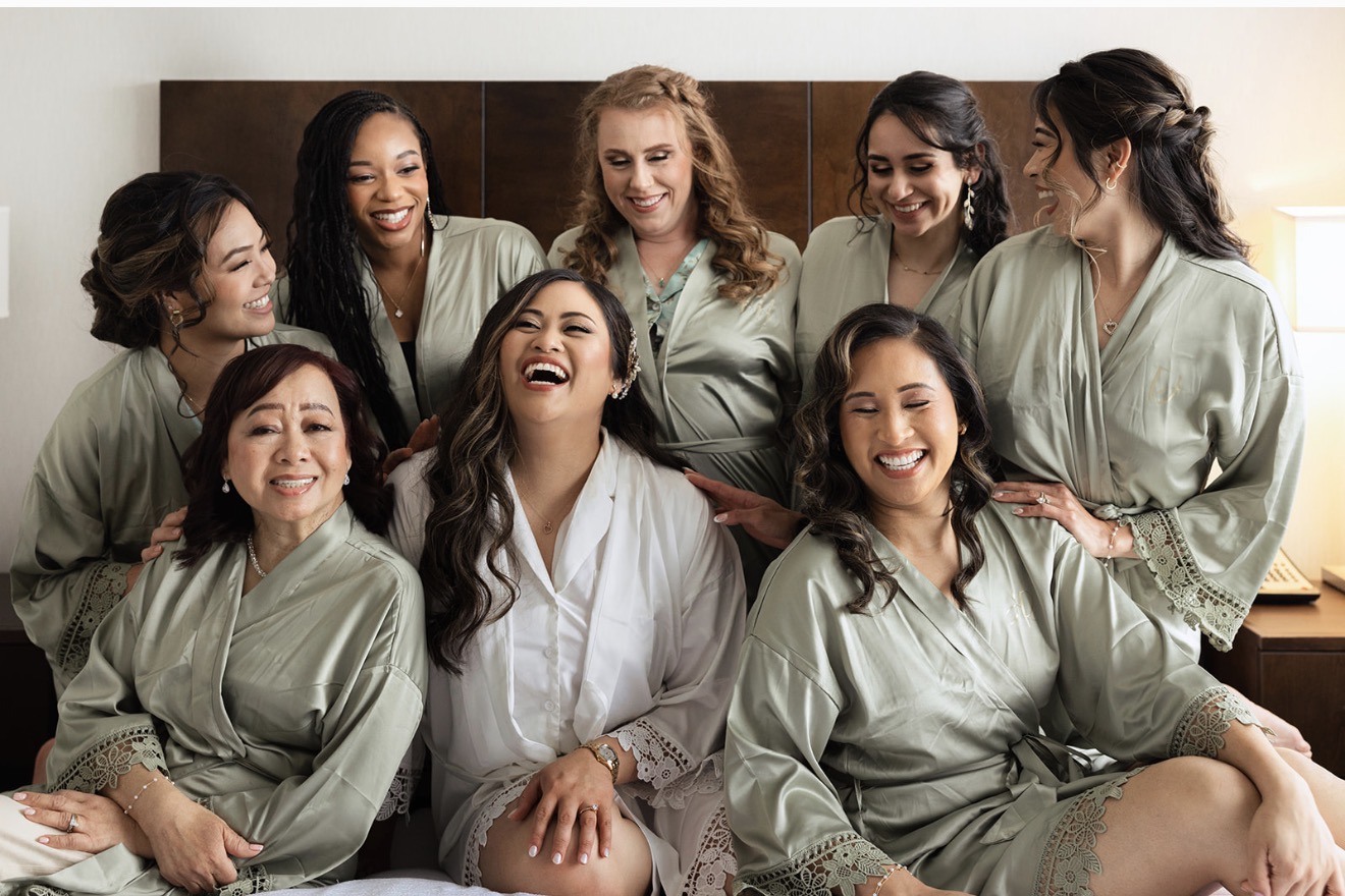 Bride and bridal party laughing together while getting ready, sage-green robes