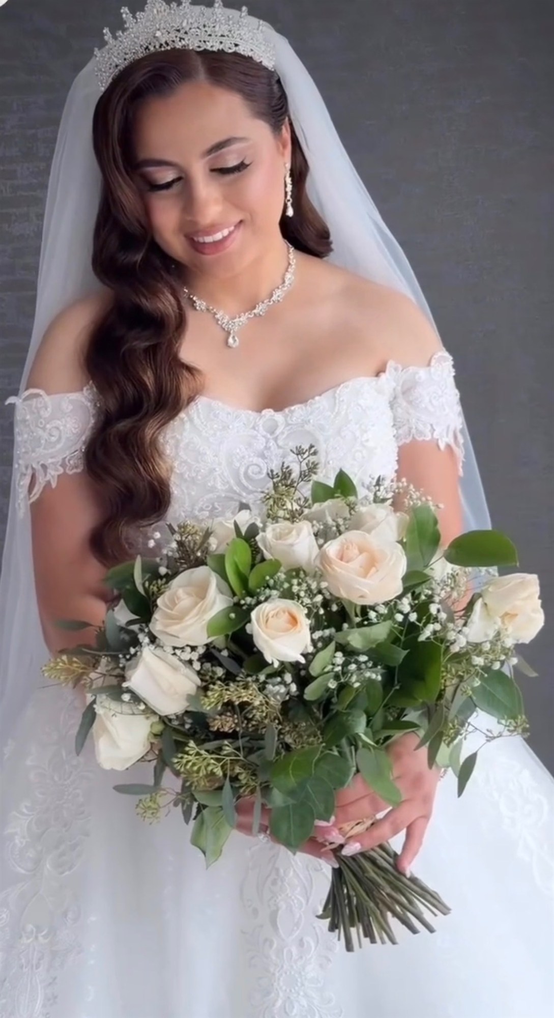 Bride in a tiara and veil holding a cream rose bouquet