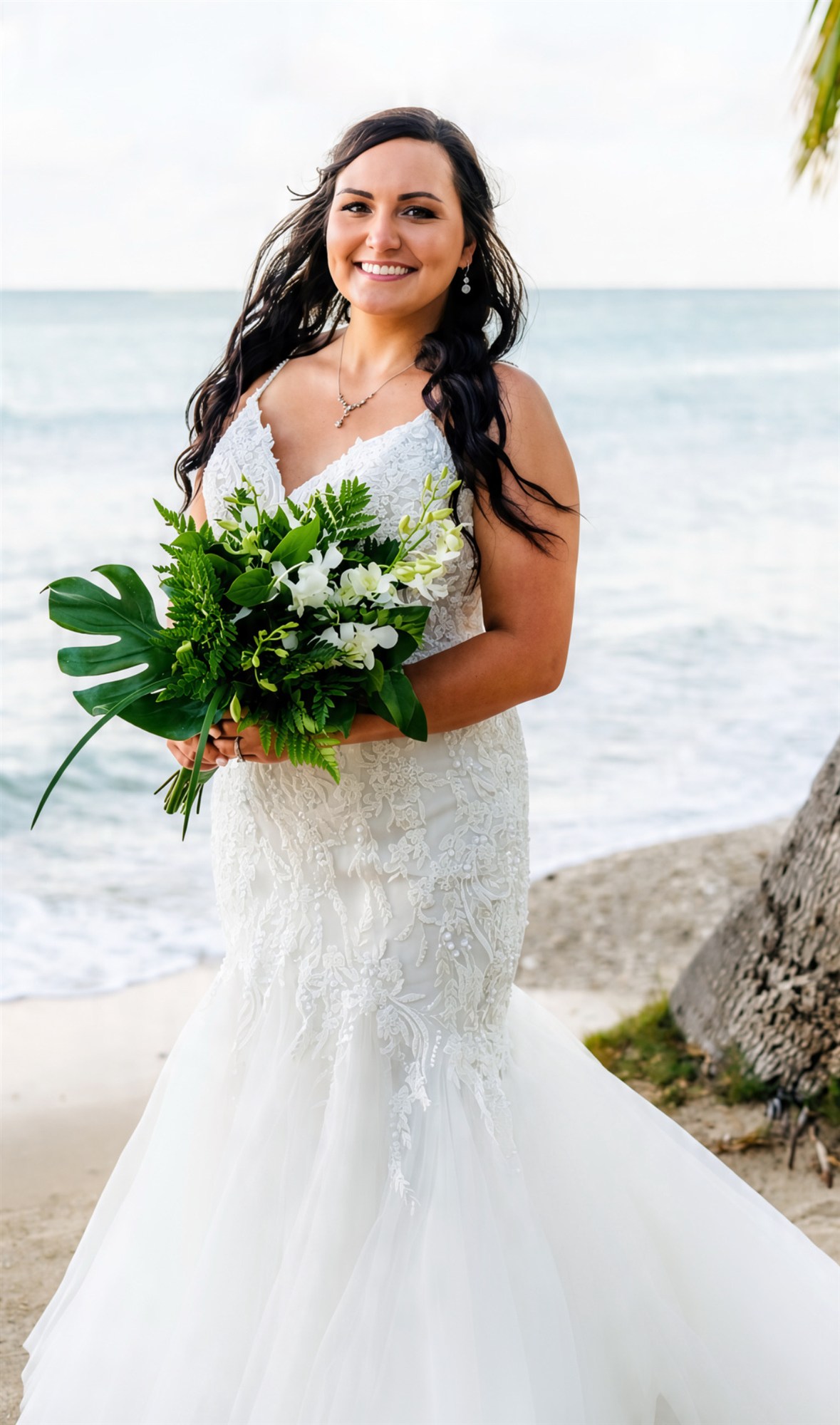 Bride in a lace mermaid gown on the beach, tropical bouquet