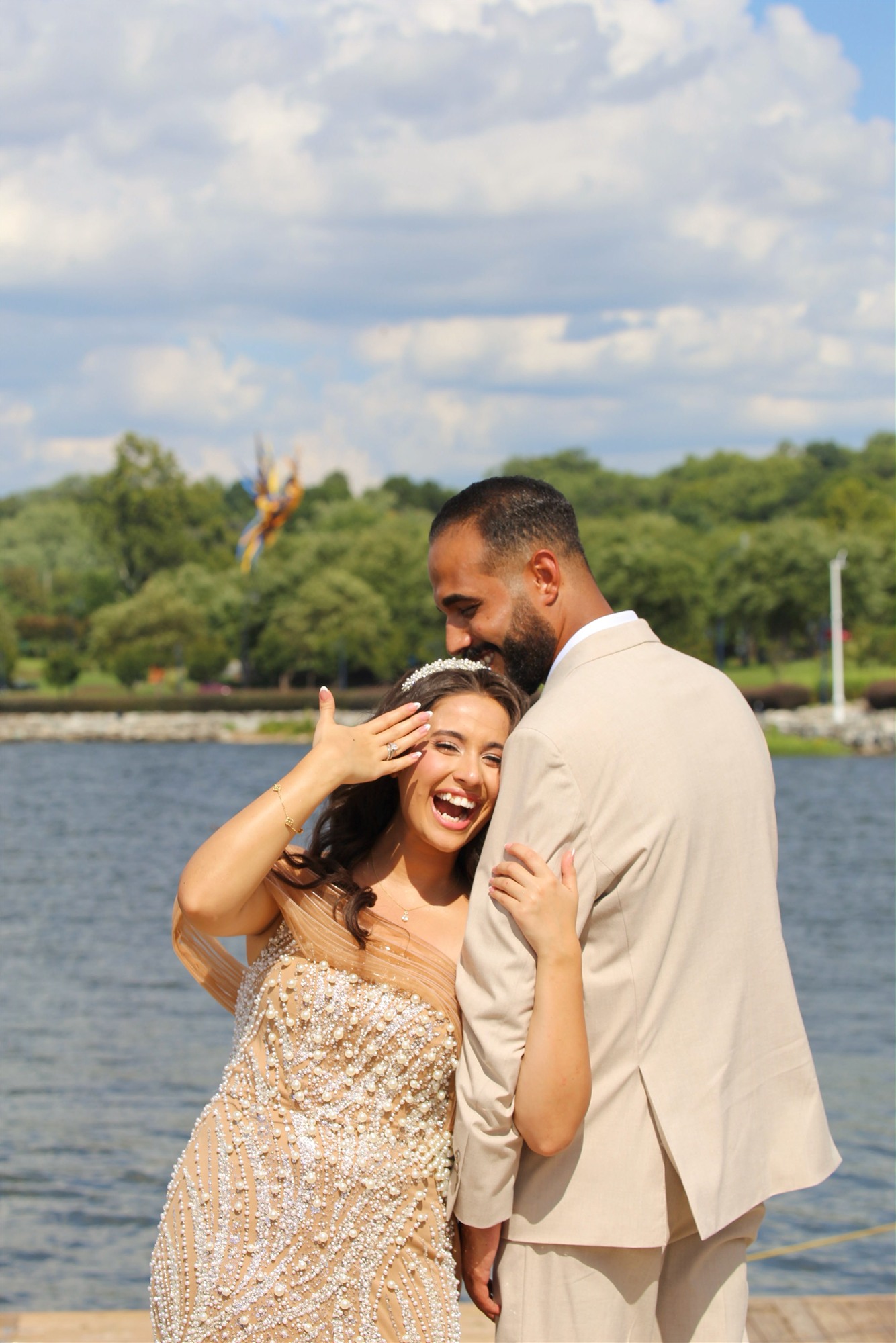 Bride and groom laughing together by the water, gold beaded gown