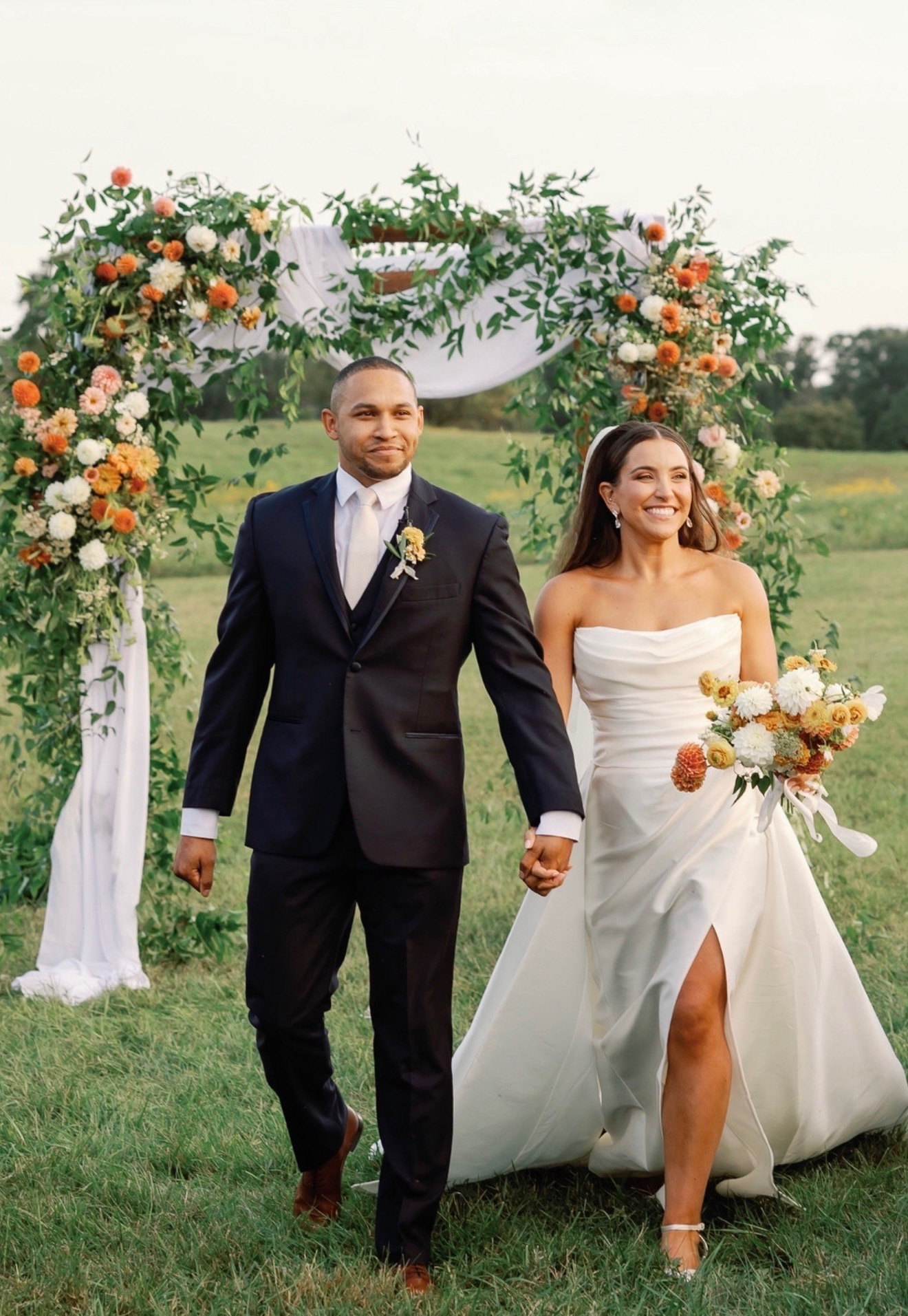 Bride and groom walking hand in hand from a floral ceremony arch