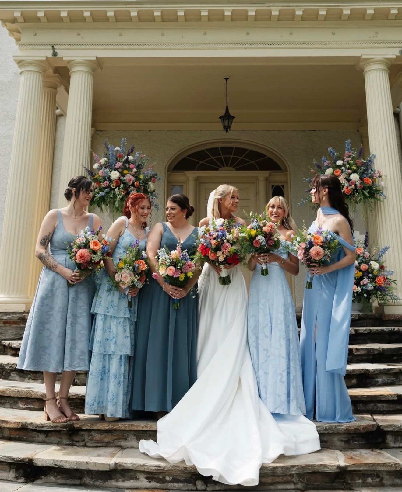 Bride with six bridesmaids in dusty-blue dresses on a mansion staircase