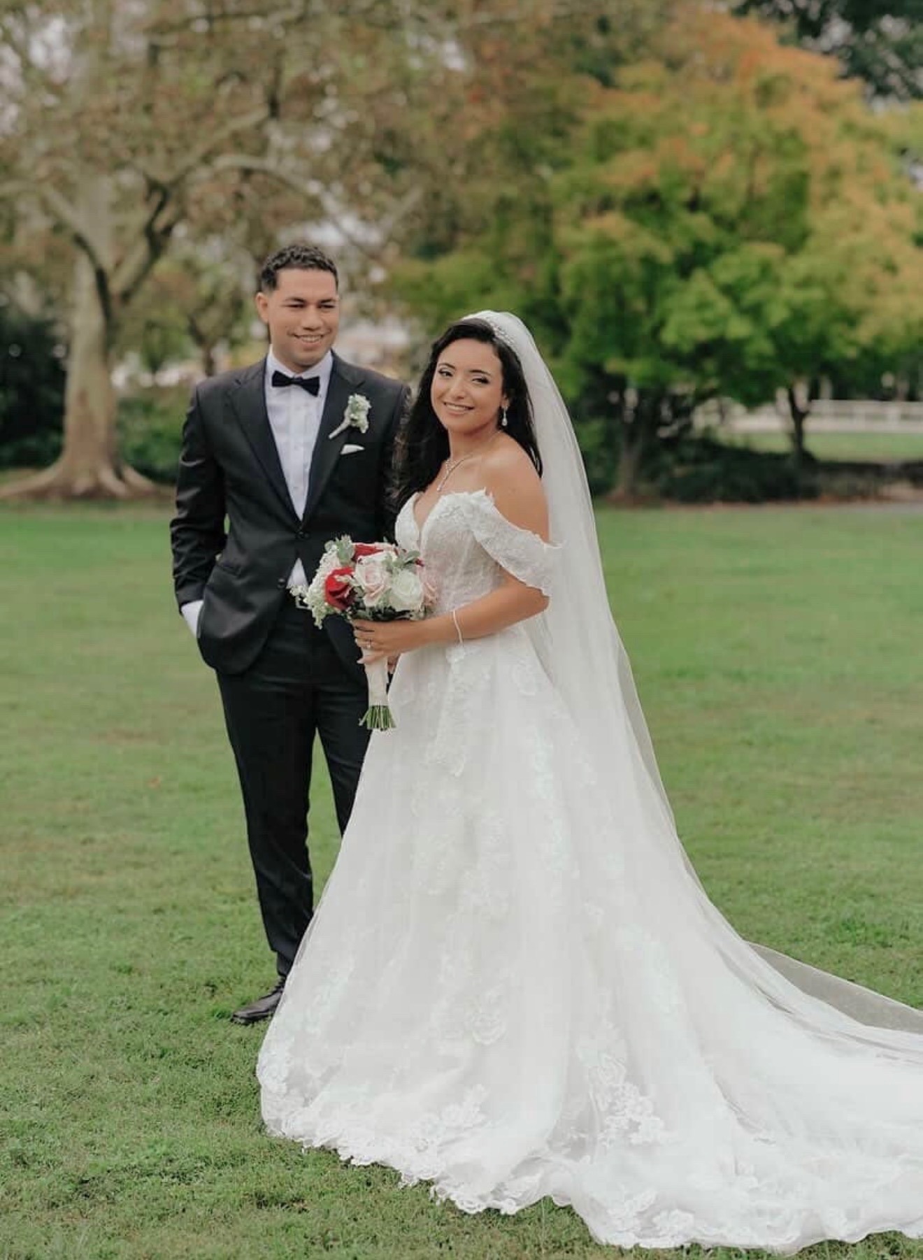 Bride and groom smiling together in a garden, red and white bouquet