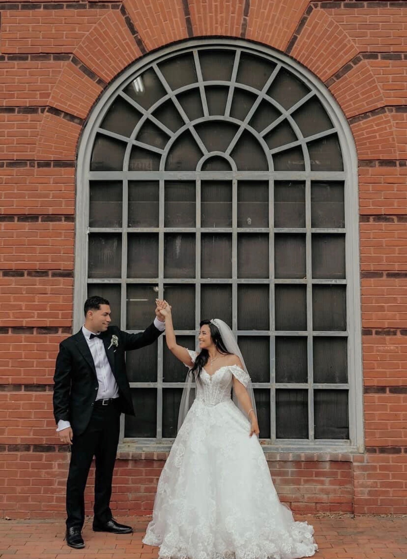 Bride and groom holding hands in front of a brick archway window