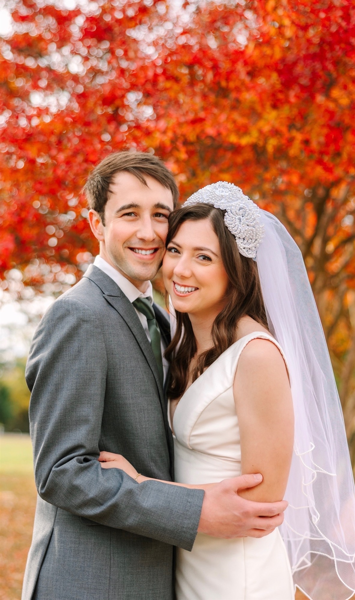 Bride and groom embracing in front of a red autumn tree