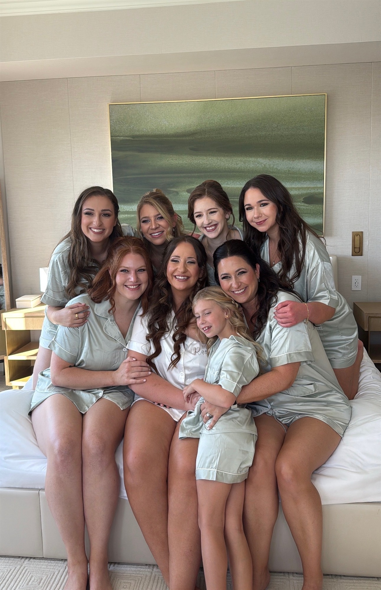 Bride with her bridal party in sage-green pajamas on a hotel bed