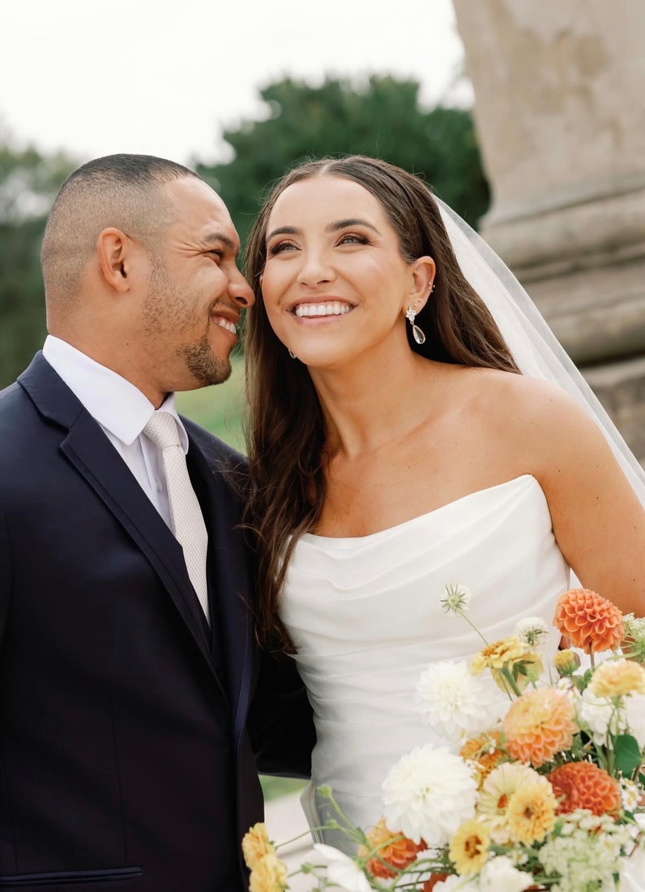 Bride and groom smiling closely together, bouquet of orange and white dahlias
