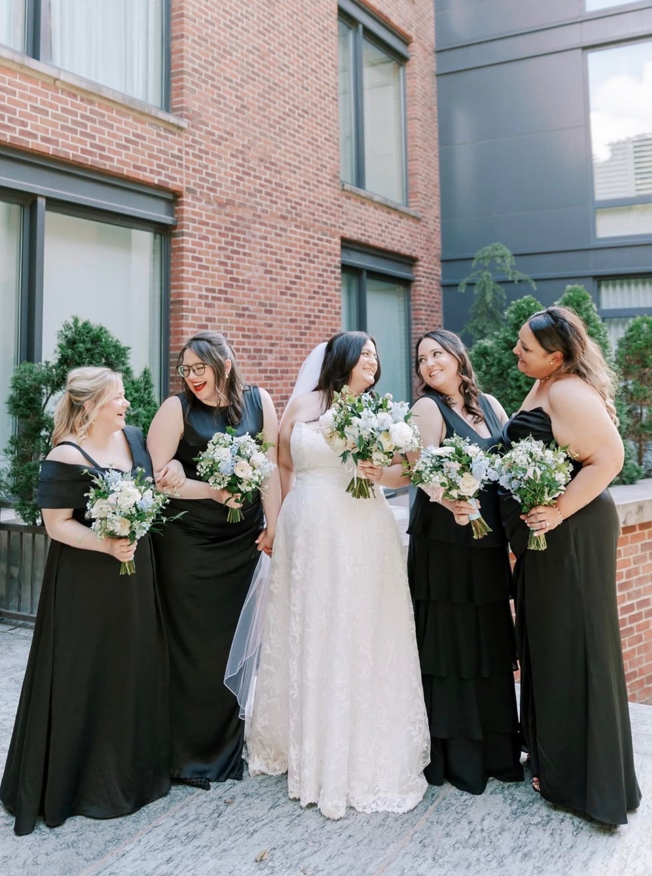 Bride with four bridesmaids in black gowns, brick courtyard