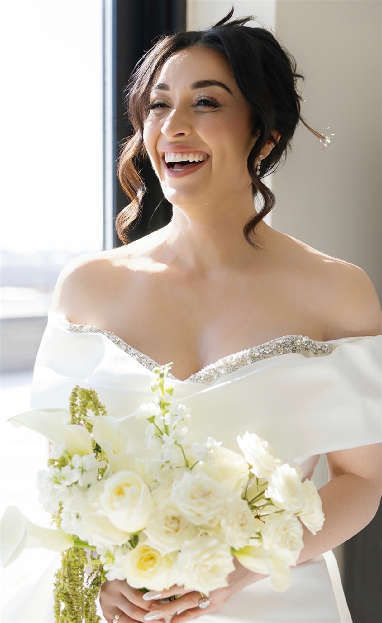 Bride laughing joyfully with her bouquet, off-shoulder gown