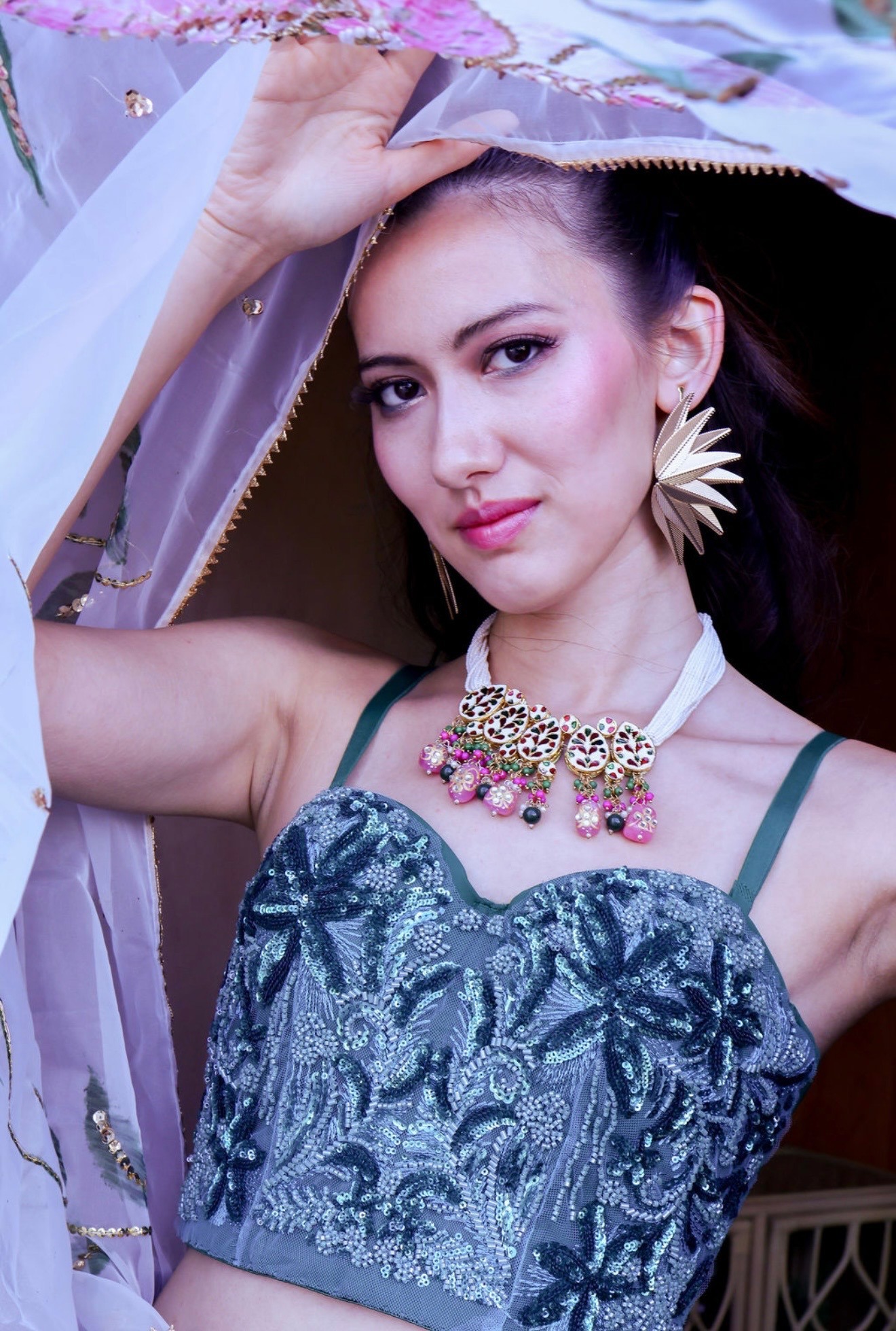 Editorial portrait in a sequined teal bustier with a veil overhead